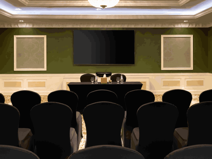 Black chairs by a head table under a large screen, surrounding Coral Room at Warwick Hotels & Resort