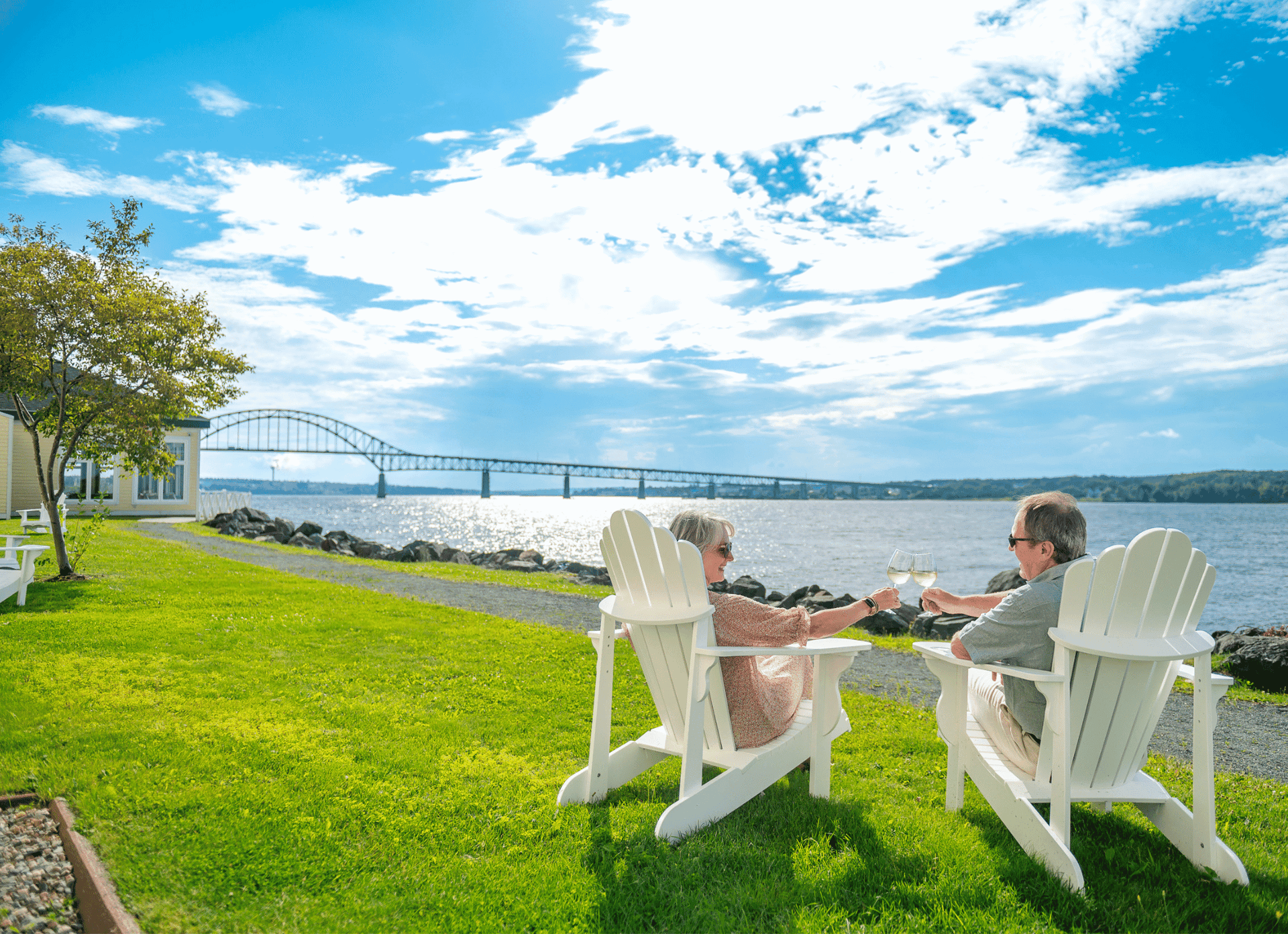 Couple sitting in lawn chairs on a grass lawn by water at Rodd Miramichi River, an apartment hotel in Miramichi, NB