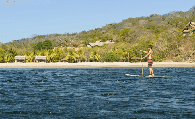 Man paddleboarding on calm water near the private beach at Morgan’s Rock, one of the hotels in San Juan del Sur