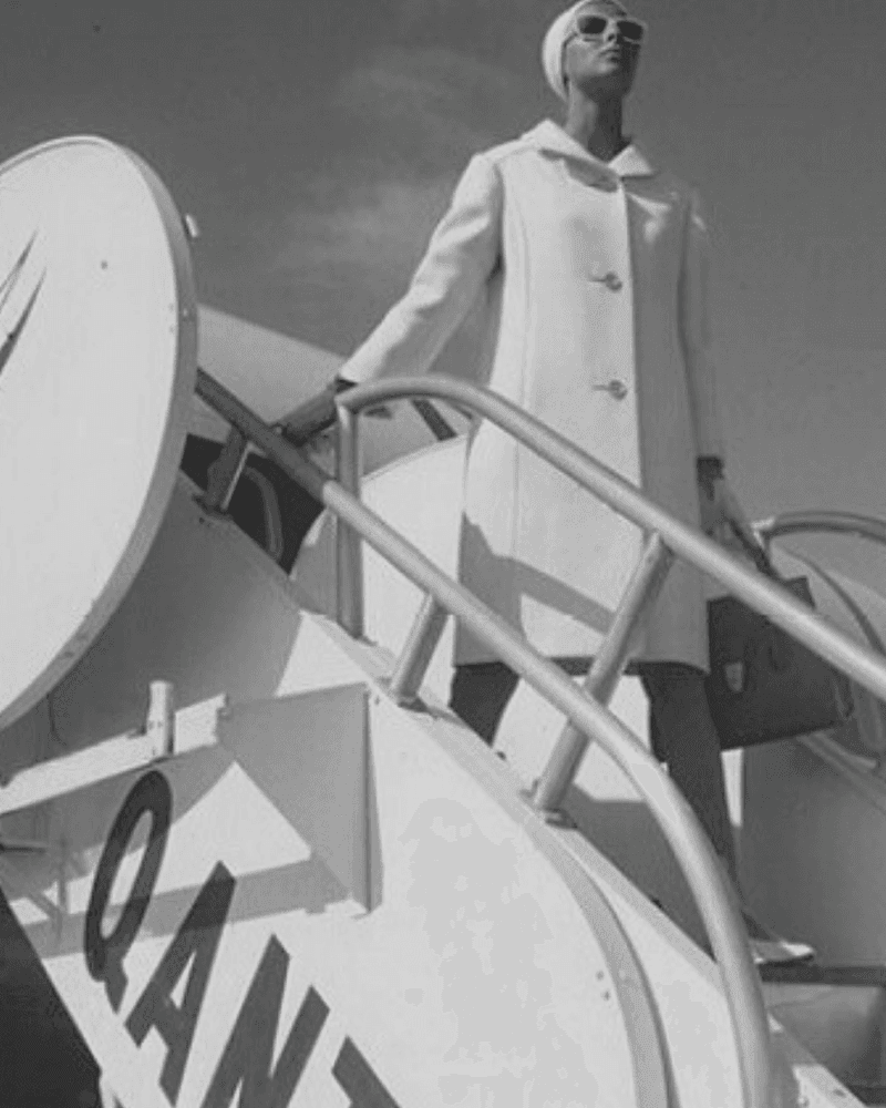 A woman in a white coat descending the Qantas aircraft stairs, holding a handbag.