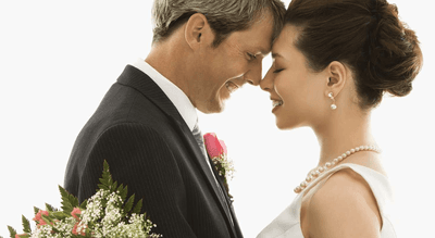 Close-up of a bride and groom smiling forehead-to-forehead, bride wearing pearls, groom in a pink boutonniere