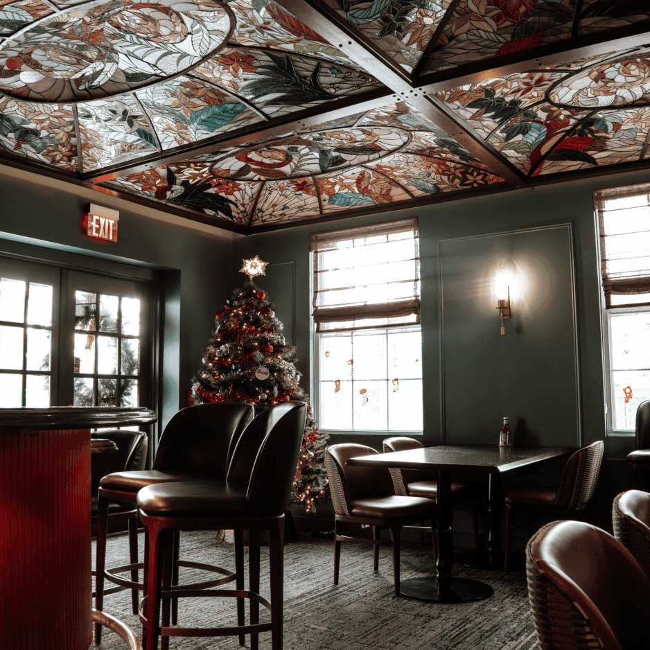 Leather chairs and tables set by a Christmas tree beneath a stained-glass ceiling at La Tourelle Inn and Spa