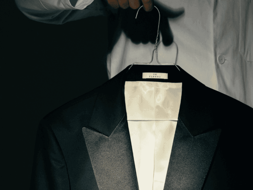 Front view of a man holding a black suit on a hanger at The Godfrey Hotel Hollywood