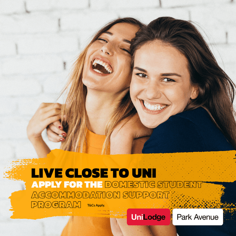 Two female students embracing against a white brick wall in a promotional image for UniLodge Park Avenue.