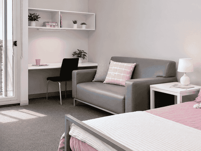 Modern studio apartment with gray sofa, desk area, and pink bedding accents at Student Living - Waymouth