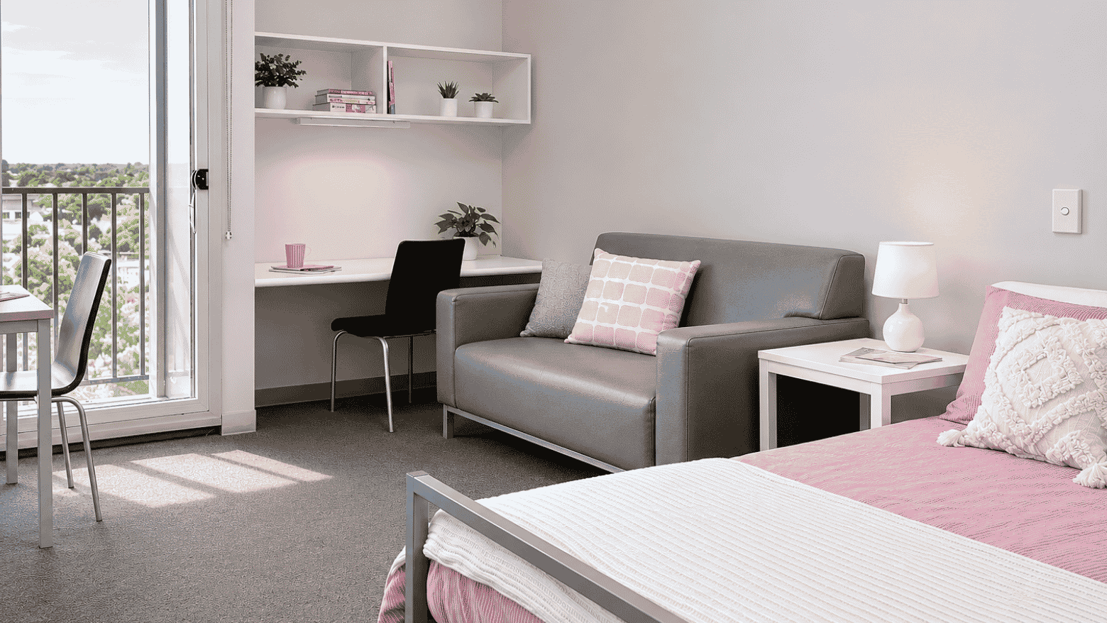 Modern studio apartment with gray sofa, desk area, and pink bedding accents at Student Living - Waymouth