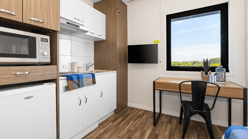 Modern room with kitchenette, desk, and large window at StudentLiving Darwin.