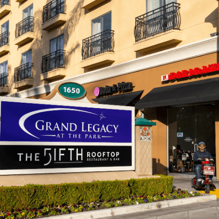 Person using mobility scooter near hotel entrance with Grand Legacy at the Park and The Fifth Rooftop signage visible