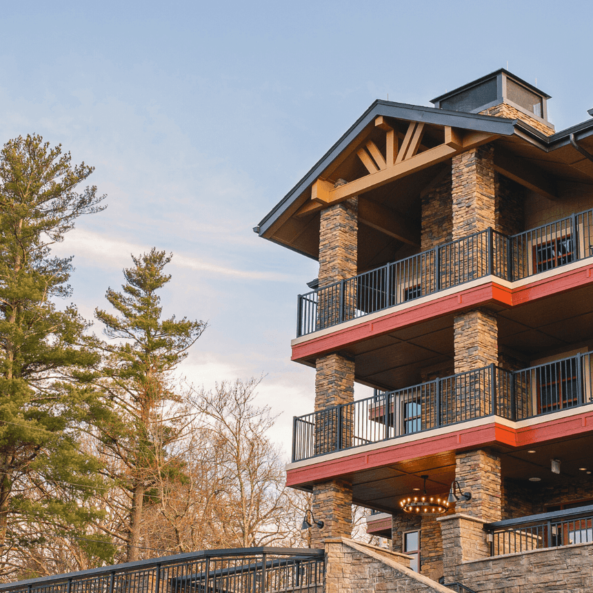 Exterior of the hotel with stone pillars, red trim, and balconies rising next to tall pine trees at The Embers Hotel
