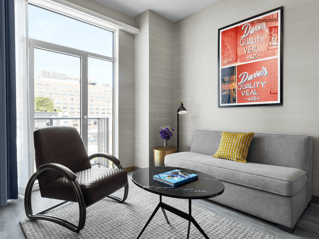 Livingroom featuring a gray sofa, leather chair, coffee table, and artwork in Gansevoort suite at Gansevoort Meatpacking NYC
