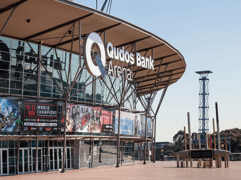 Front view of the Quodos Bank Arena with banners on the side and a tower in the background.