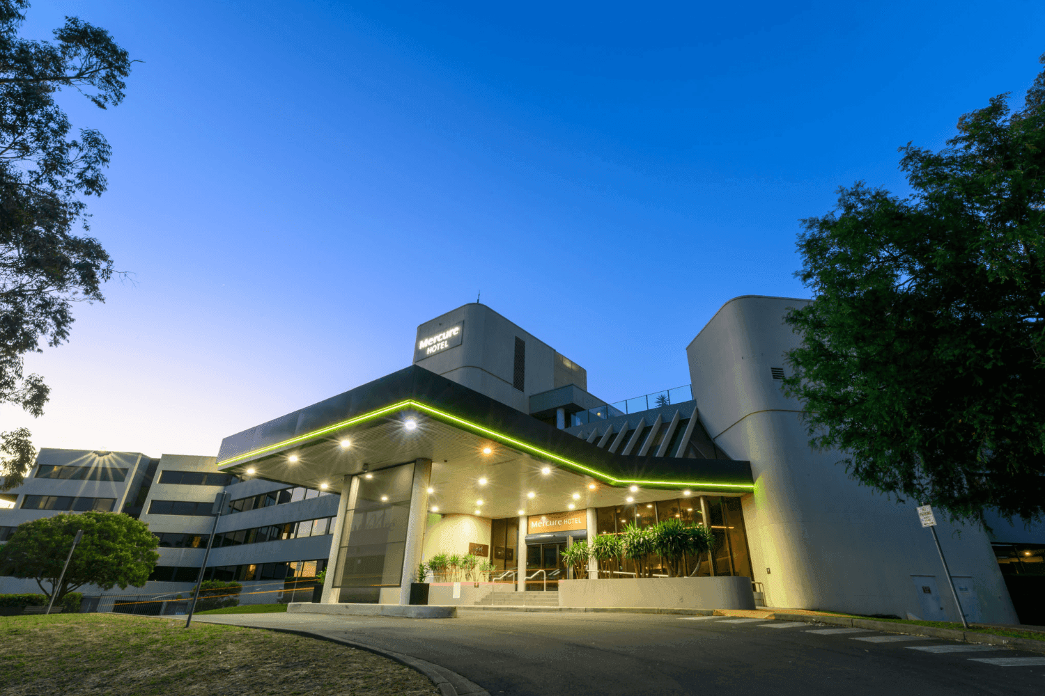 Dusk view of Mercure Penrith hotel entrance with lit signage and trees at Mercure Penrith
