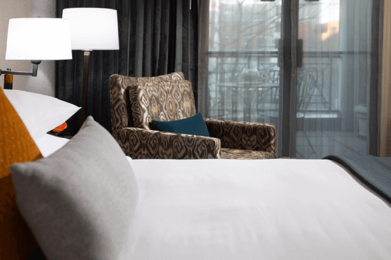 A hotel room with a bed, chair, lamp, and balcony