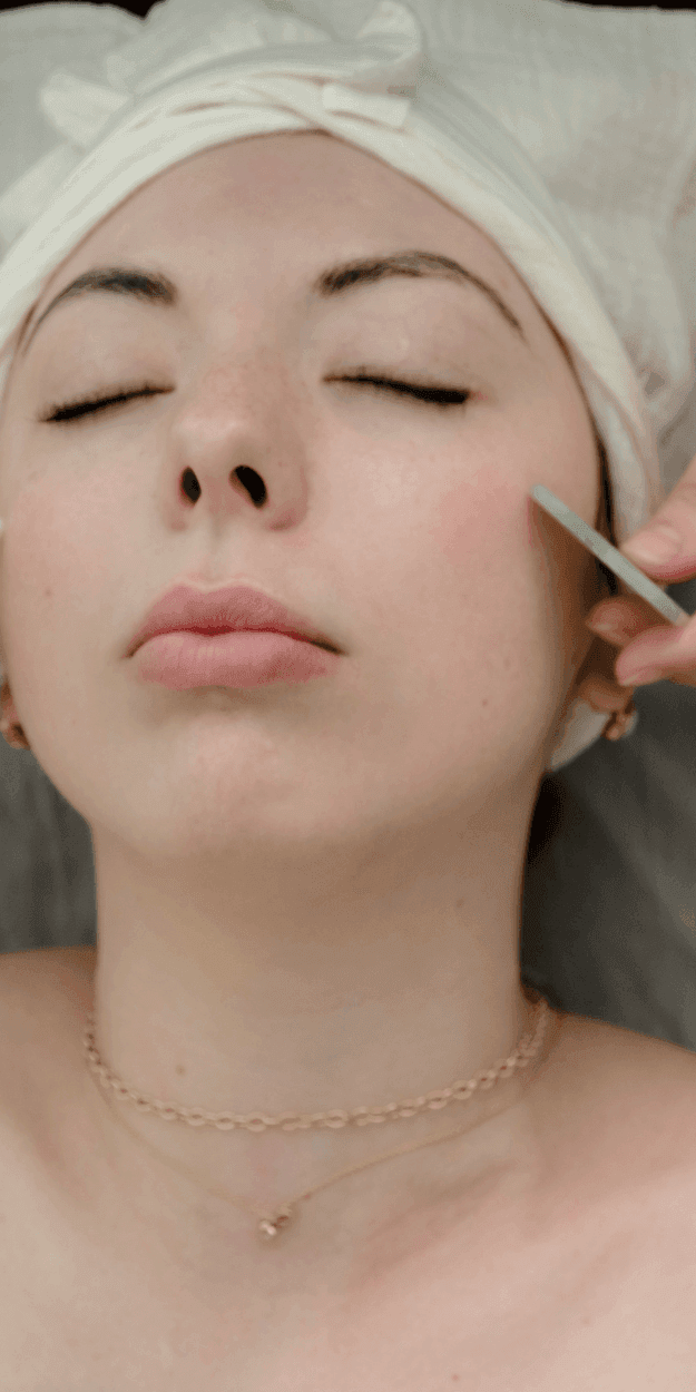 Guest with towel wrap receiving a facial treatment, esthetician applying tool near her cheek at La Tourelle Inn & Spa