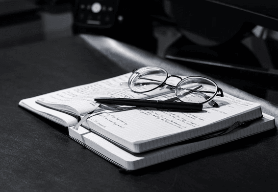 Two opened notebook lying on the table with a pen and a spec glass 