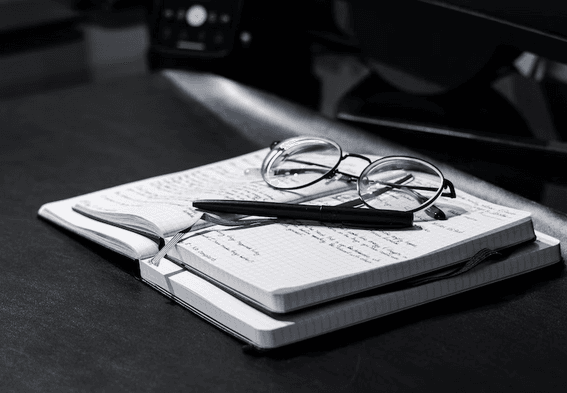 Two opened notebook lying on the table with a pen and a spec glass