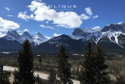 View of snow-capped Three Sisters mountains under a bright blue sky with scattered clouds seen from Falcon Crest Lodge