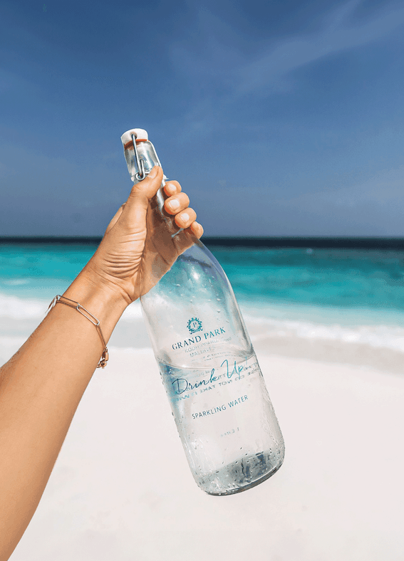 A person at the beach holds a bottle of water at Grand Park Kodhipparu, Maldives