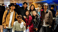 Group of seven young students smiling together in a lively indoor social space with UniLodge branding.