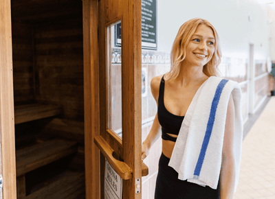 Woman with a striped towel standing beside the open wooden sauna in the pool area at Rodd Crowbush Golf & Beach Resort