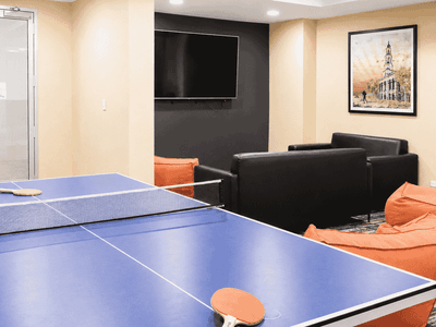 Modern recreation room with ping pong table, black leather sofa, orange bean bags, and wall-mounted television.