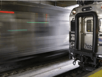 Moving train blurred in motion beside a stationary train car at a platform near APA Hotel Woodbridge