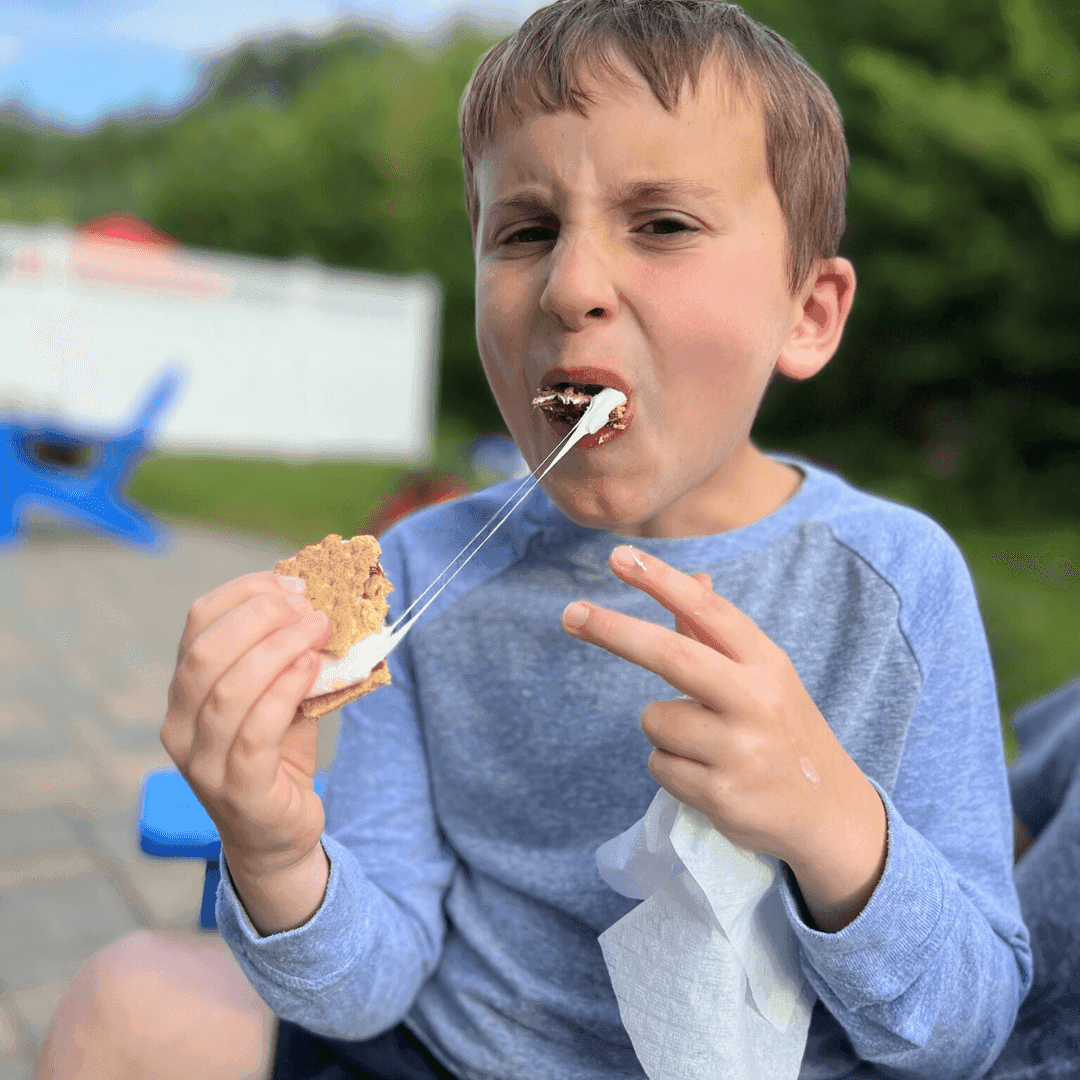 A young boy bitting into a s'mores with a gooey melted marshmallow
