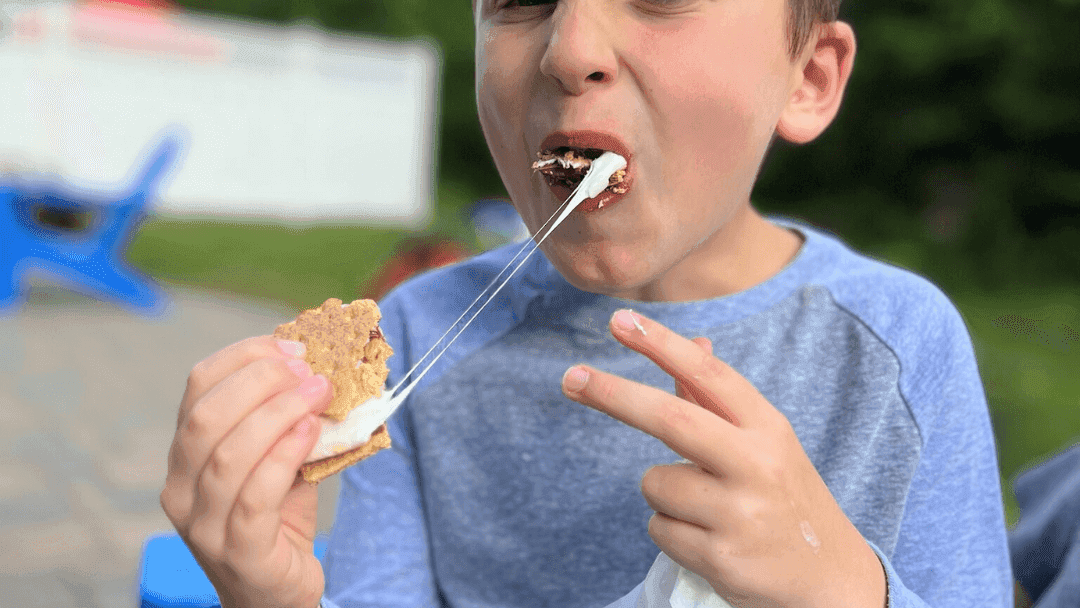 A young boy bitting into a s'mores with a gooey melted marshmallow 