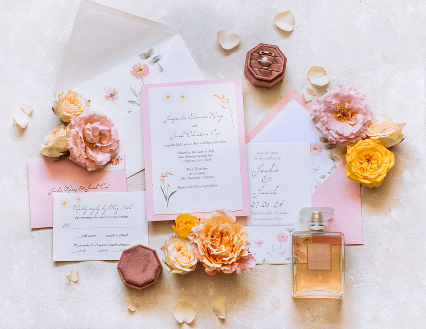 Wedding invitations at The Clifton Hotel in Charlottesville, VA, with flowers, rings, and perfume arranged on a table.
