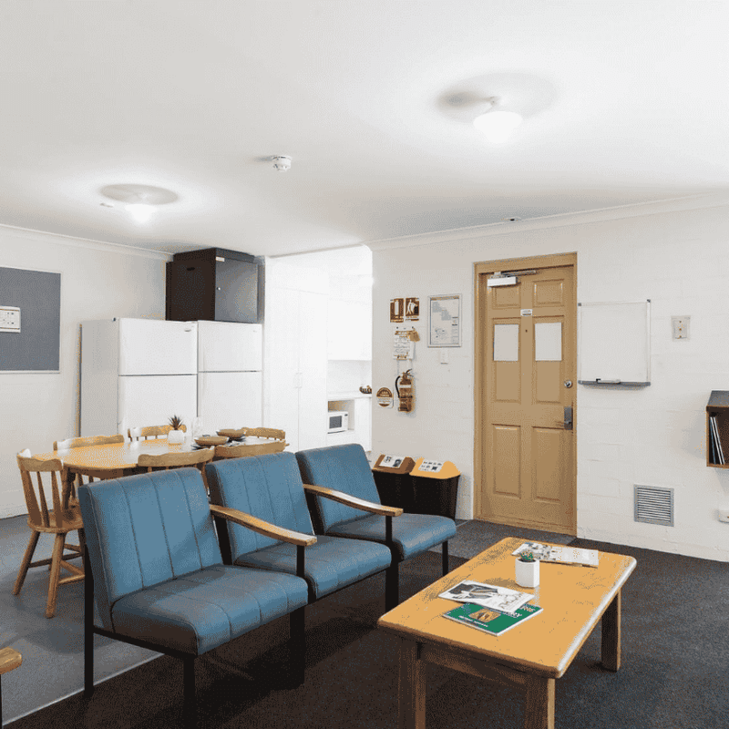 Comfortable lounge area with blue chairs, a wooden table, and a bulletin board at UniLodge at Curtin University - Vickery House.