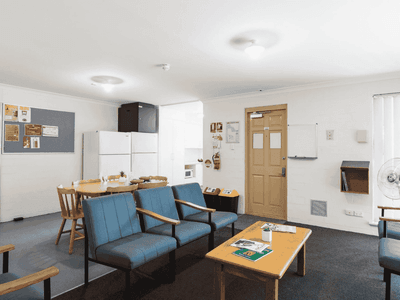 Comfortable lounge area with blue chairs, a wooden table, and a bulletin board at UniLodge at Curtin University - Vickery House.