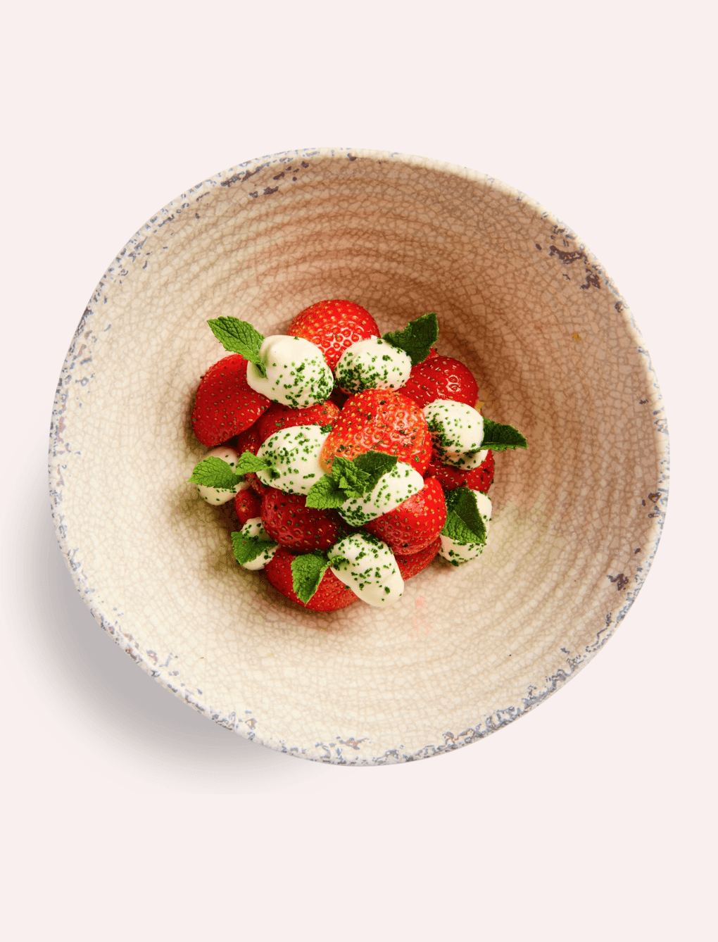 Decorative bowl filled with fresh strawberries topped with cream and vibrant green mint leaves served at The Londoner Hotel