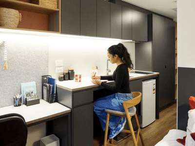 Woman sitting at a small kitchen counter writing with a pen in a compact living space.