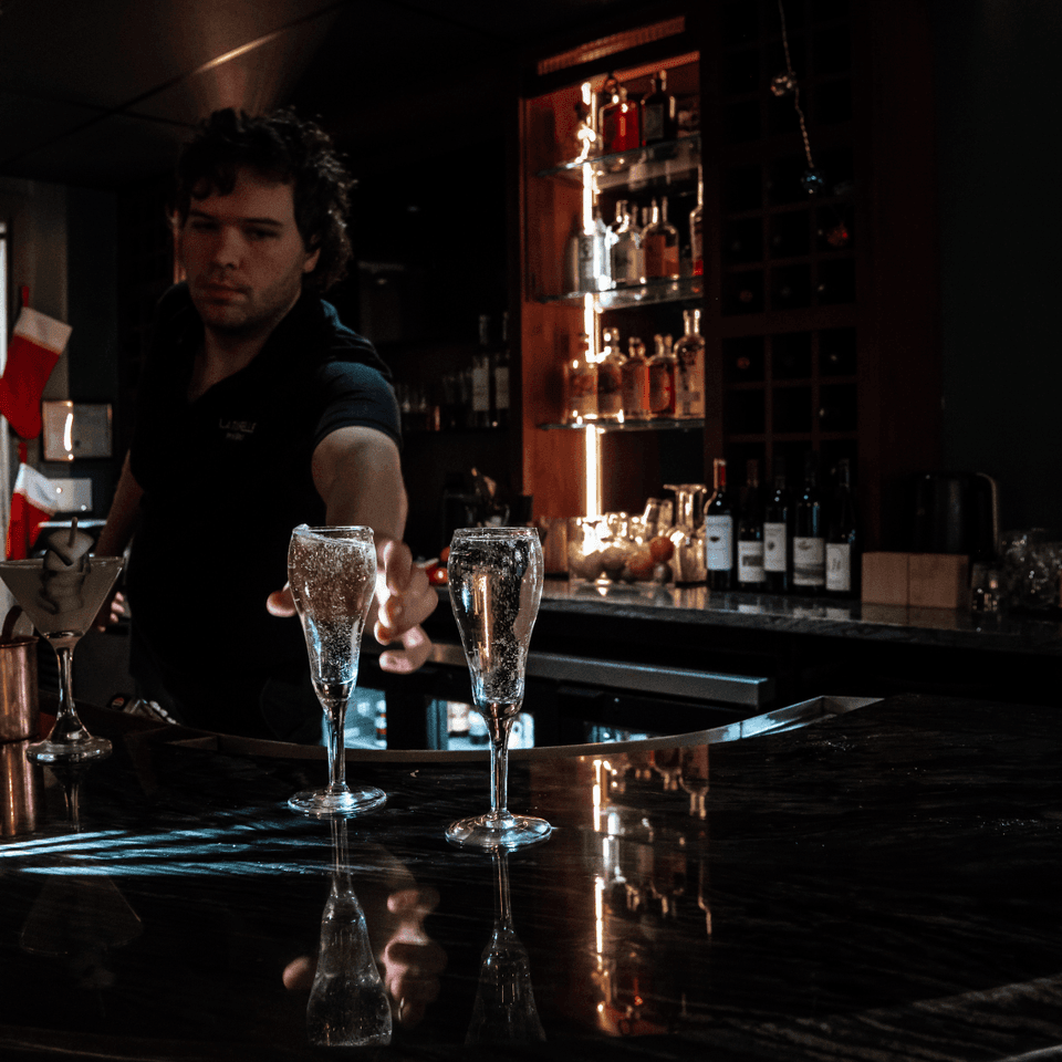 Bartender reaching for champagne flutes by a glowing shelf of liquor bottles at the bar in La Tourelle Inn and Spa