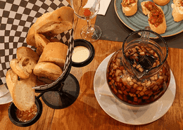 Glass pitcher of fruit sangria beside a basket of sliced bread with assorted appetizer dips at Unika Hotels