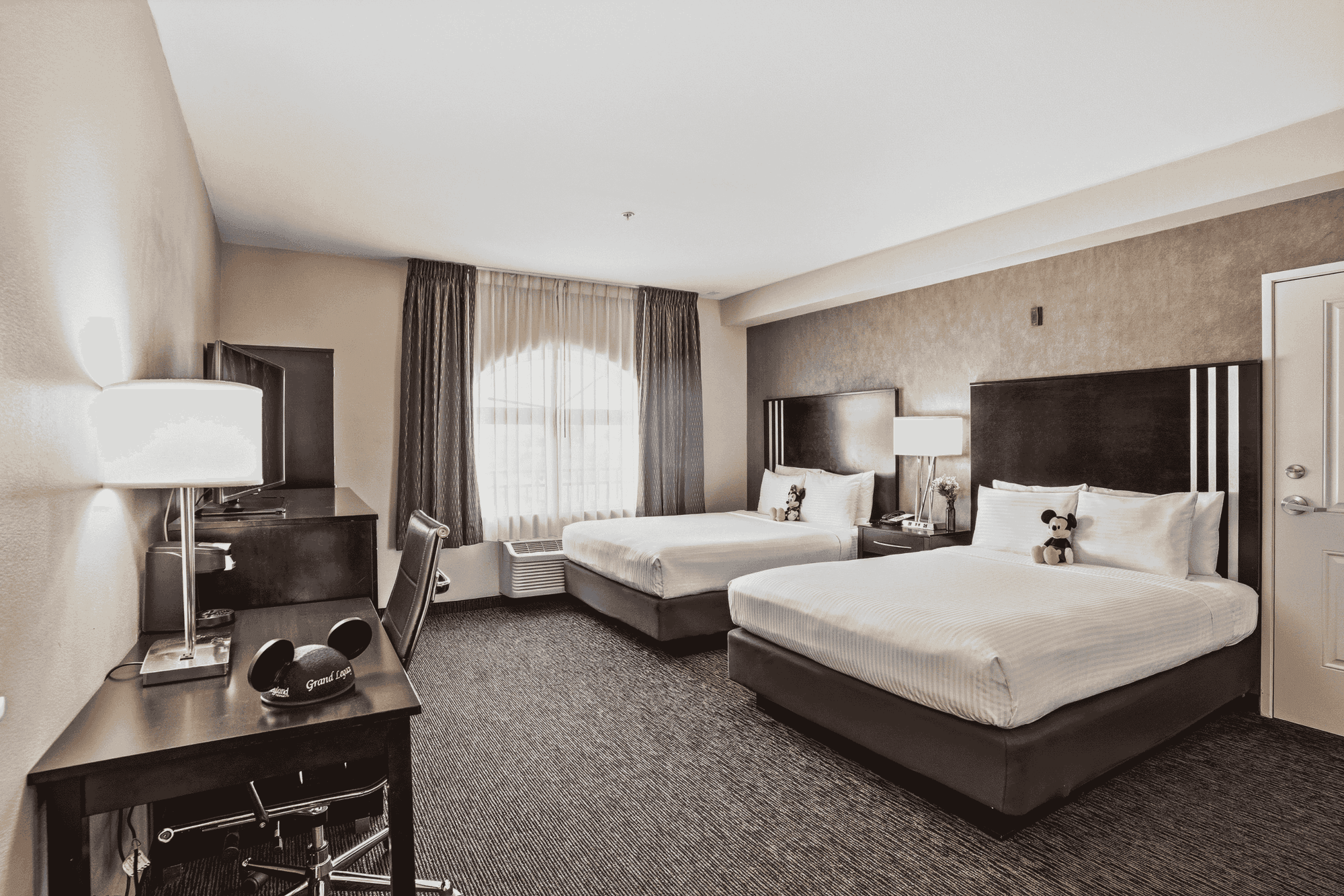 A hotel room with two beds, a desk, and a window