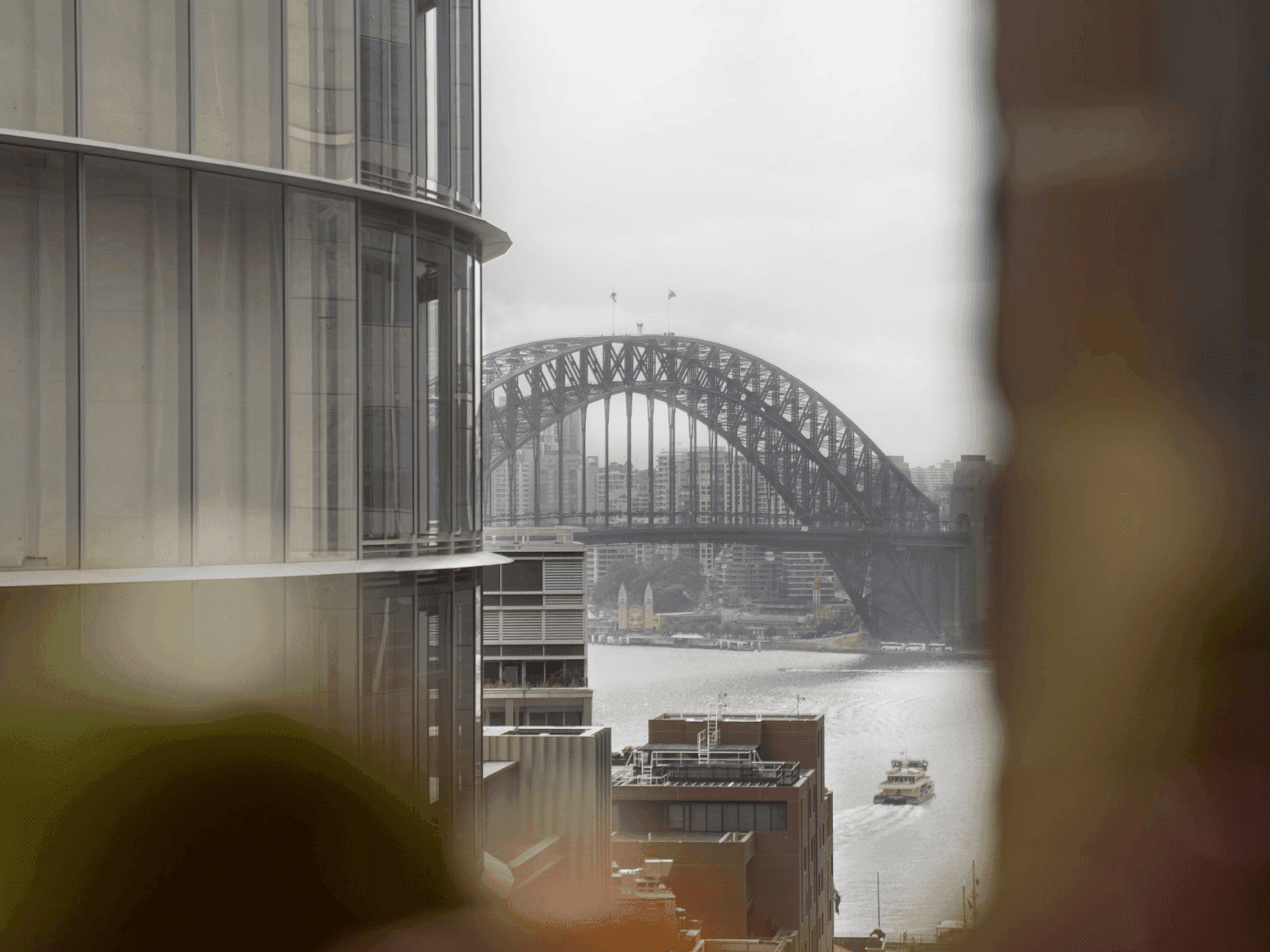 A view from a window shows a city skyline with a large arch bridge and buildings in the foreground.