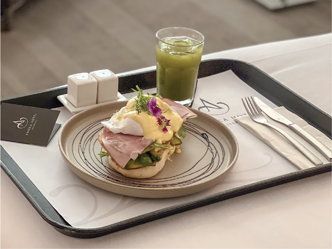 A finely plated sandwich & green juice on a tray at Amora Hotel