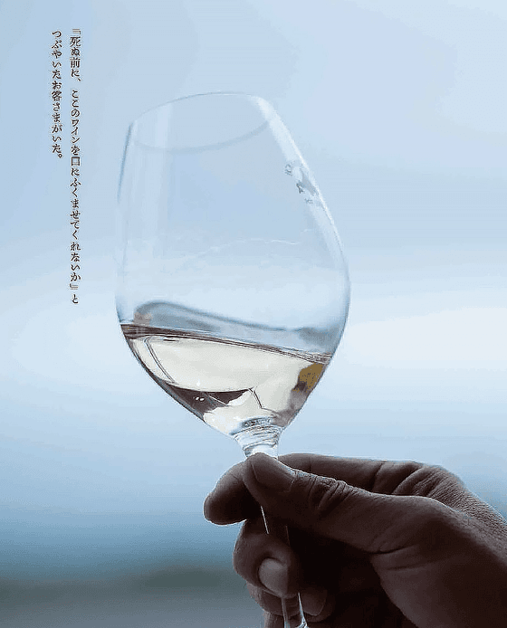 A hand holding a glass of wine against a blue background at The Okura Prestige Bangkok