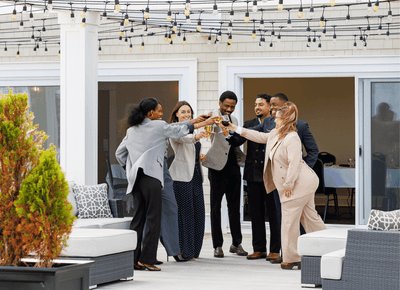 Guests toasting with wine on a patio under string lights beside wicker seating at Rodd Crowbush Golf & Beach Resort