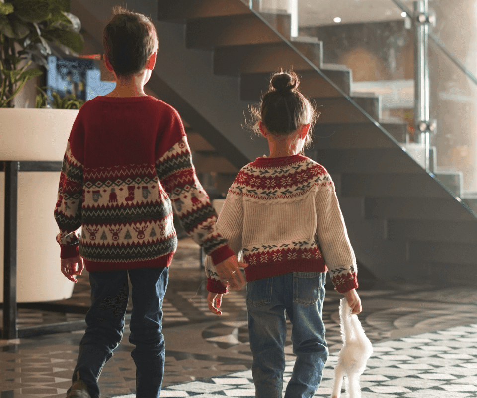 Two children in festive sweaters walking hand in hand through the bright lobby interior at Hotel X Toronto