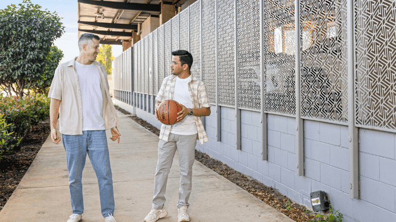 Two men chatting on a concrete walkway with a patterned wall at StudentLiving Darwin.