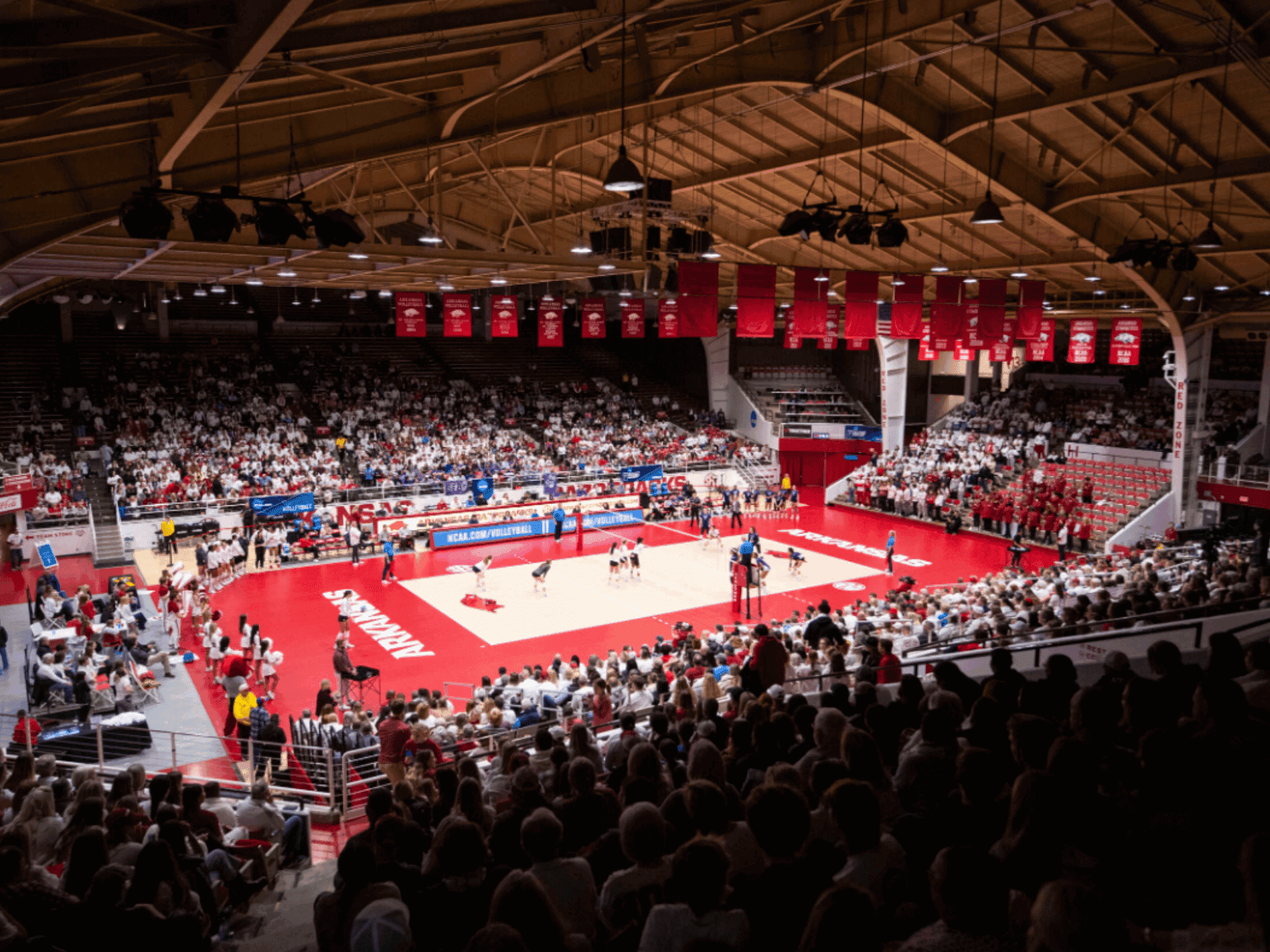 Packed indoor sports arena with red and white court, spectators, and red banners hanging from the ceiling.
