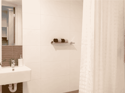 Modern bathroom with white sink, mirror, shelf with towels, shower curtain, and small plant at Student Living Waymouth