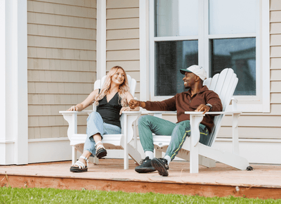 Couple relaxing on white Adirondack chairs by large exterior windows on a deck at Rodd Crowbush Golf & Beach Resort