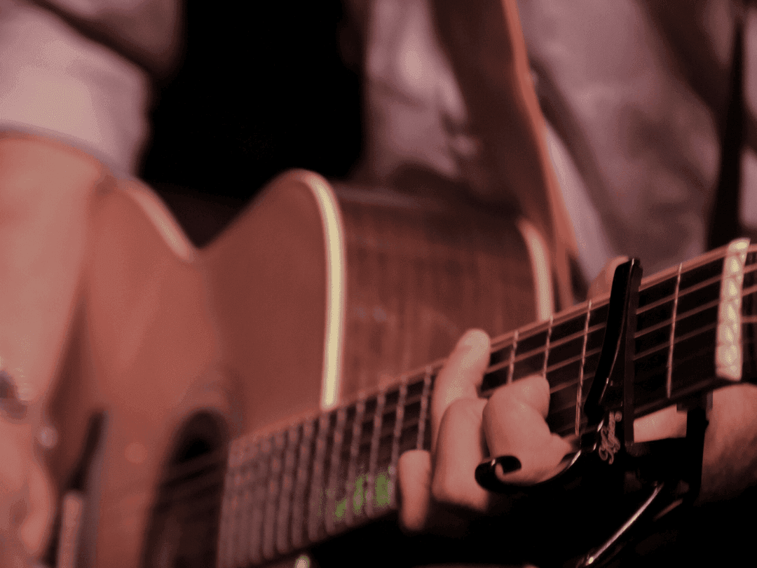 Man in white shirt playing acoustic guitar with capo attached to fretboard.