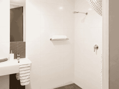 Modern white bathroom with wall-mounted sink, mirror, and accessible shower with grab bars at Student Living - Waymouth
