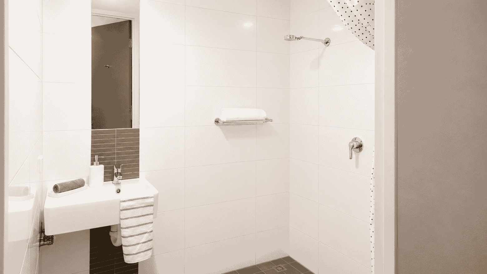 Modern white bathroom with wall-mounted sink, mirror, and accessible shower with grab bars at Student Living - Waymouth