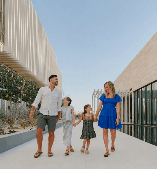Family of four walking hand in hand along modern architectural pathway at The Club at Solaz