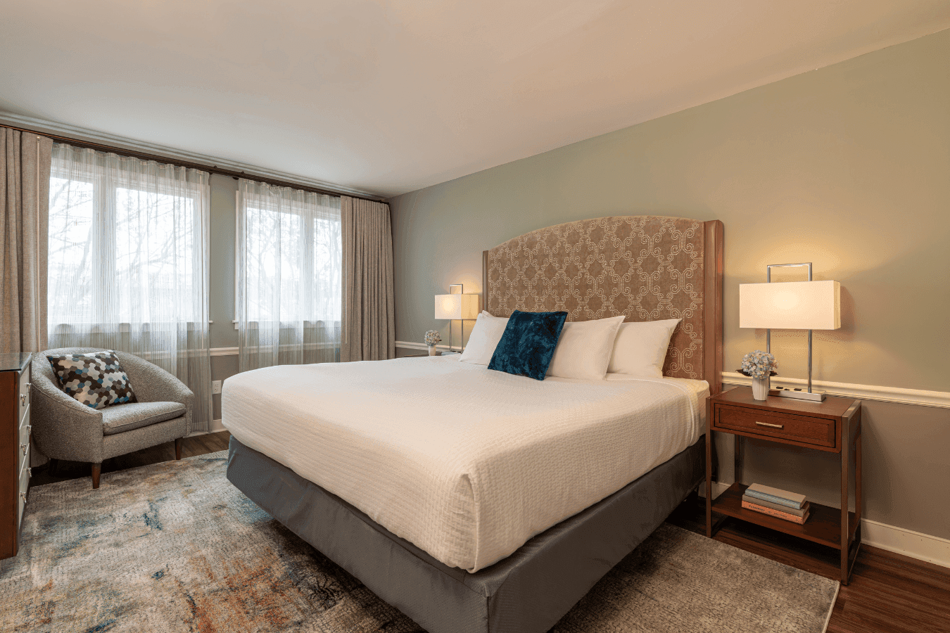 Guest room with a patterned headboard bed beside nightstand lamps and sheer window curtains at La Tourelle Inn and Spa
